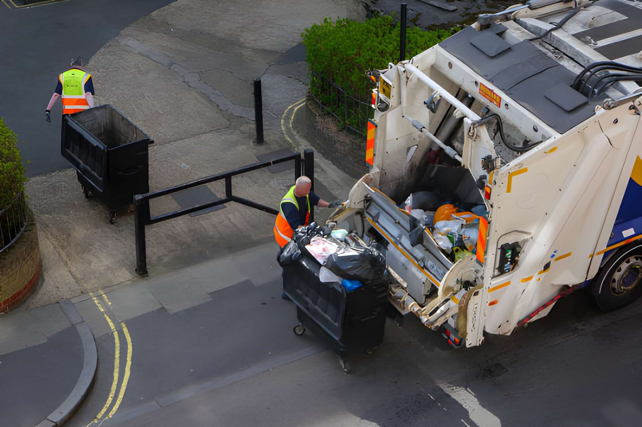 Sanitation workers loading a garbage truck on street.